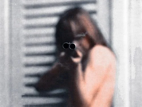 A person with long hair wearing glasses holding a gun and pointing it towards the camera