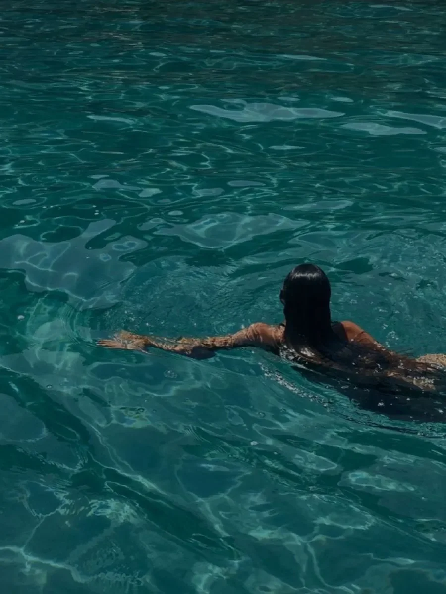 A woman swimming in the ocean with her arms extended, seen from behind.