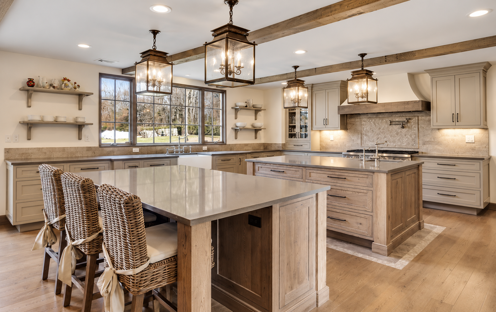 Modern kitchen with beige cabinetry, island with a wood base, wicker chairs with ribbons, large windows showing a yard, and three large hanging light fixtures.