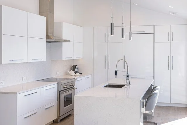 Modern white kitchen with cabinets, a central island, stainless steel appliances, and pendant lighting.