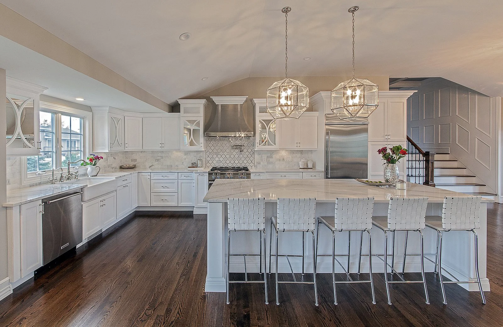 Modern kitchen with white cabinets, marble countertops, dark hardwood floors, a large island with white woven barstools, and pendant lighting