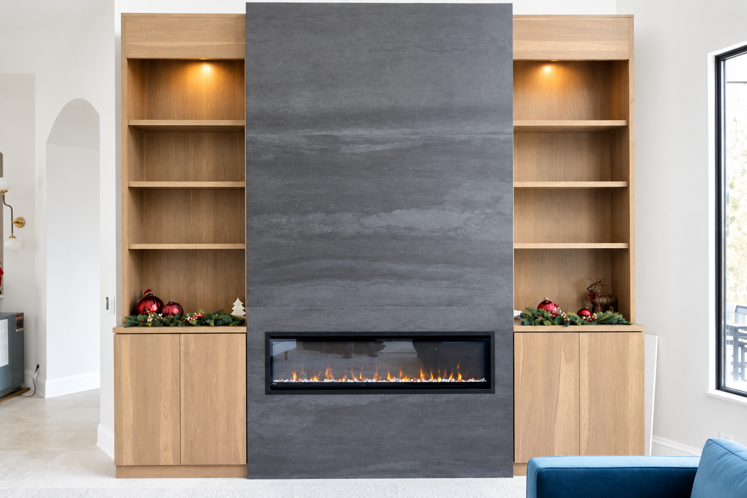 Modern living room with a central gray stone fireplace and built-in wooden shelves decorated with Christmas ornaments.