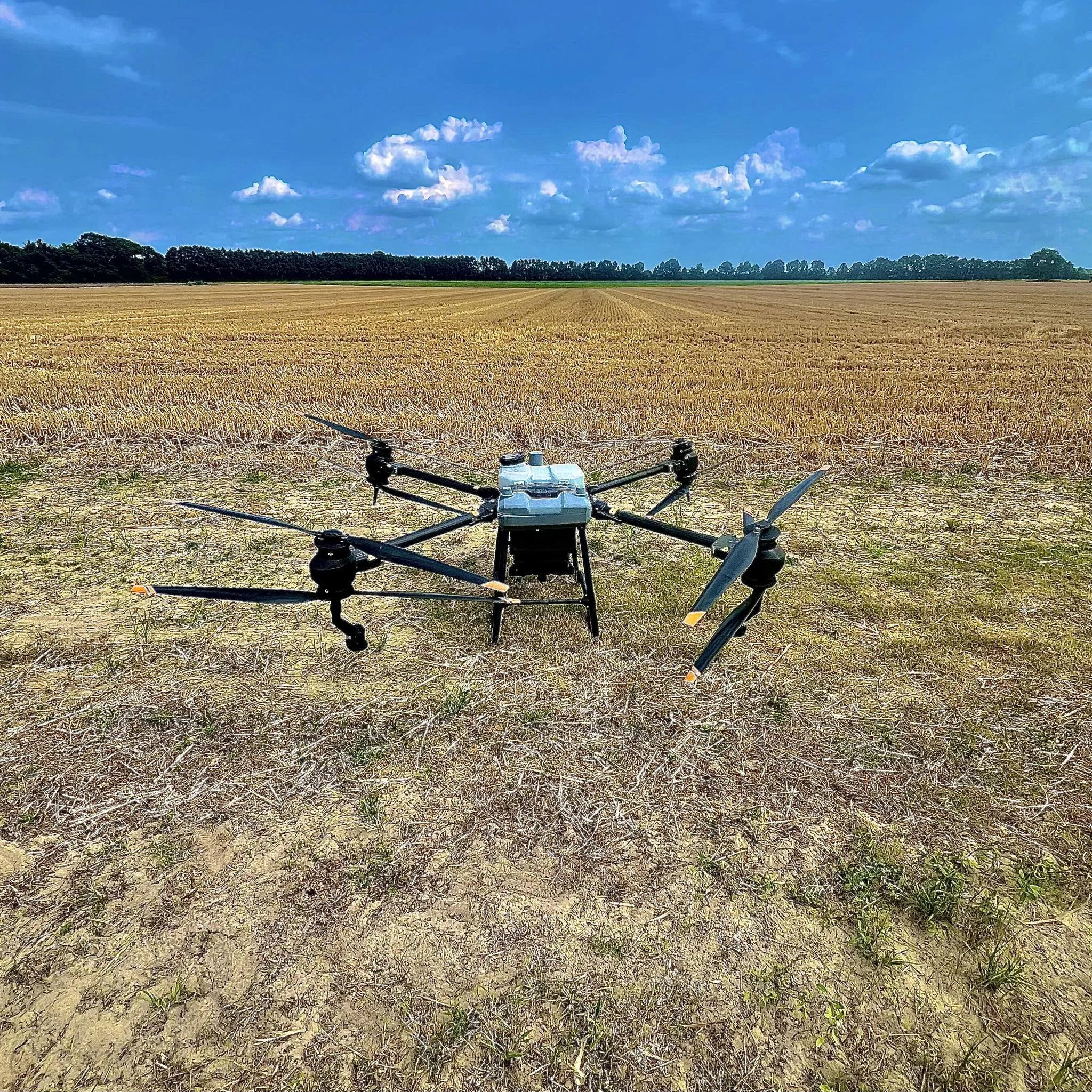 A drone flying over a harvested wheat field with a blue sky and some clouds in the background.