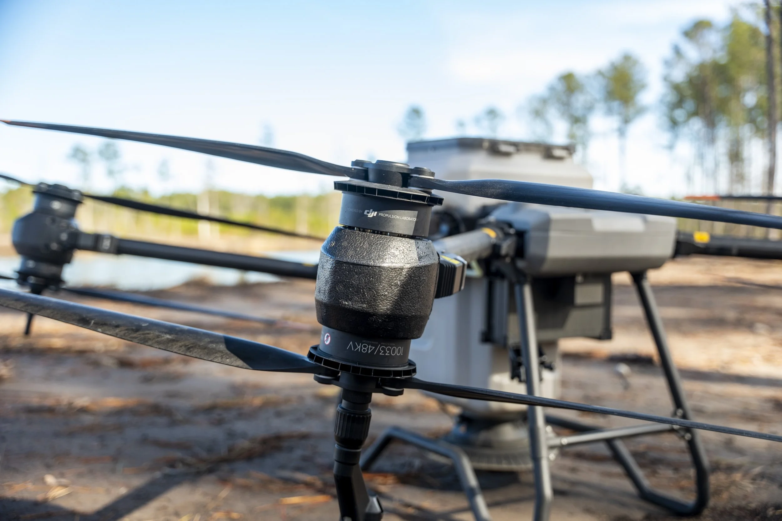 A drone propeller mounted on a drone frame outdoors with trees in the background.