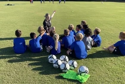 Impact FC coach talking with young players seated on the field