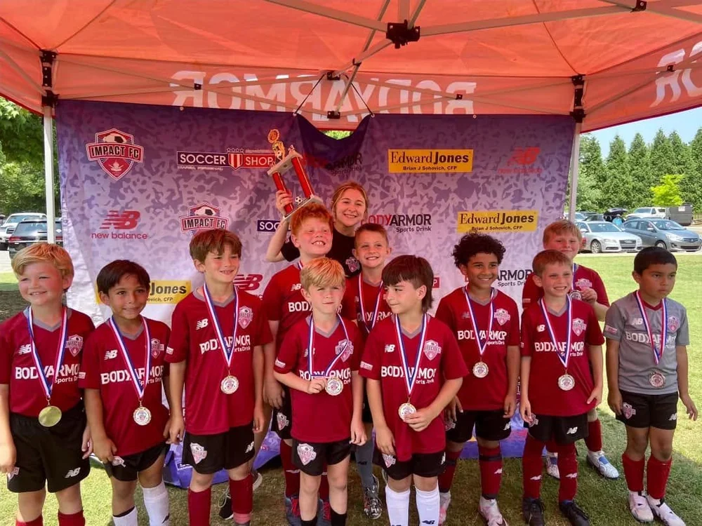 Impact FC players celebrating a Crossroads Classic win with their medals and trophy
