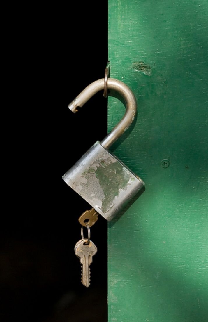A padlock securing a green door with a key hanging from the lock.