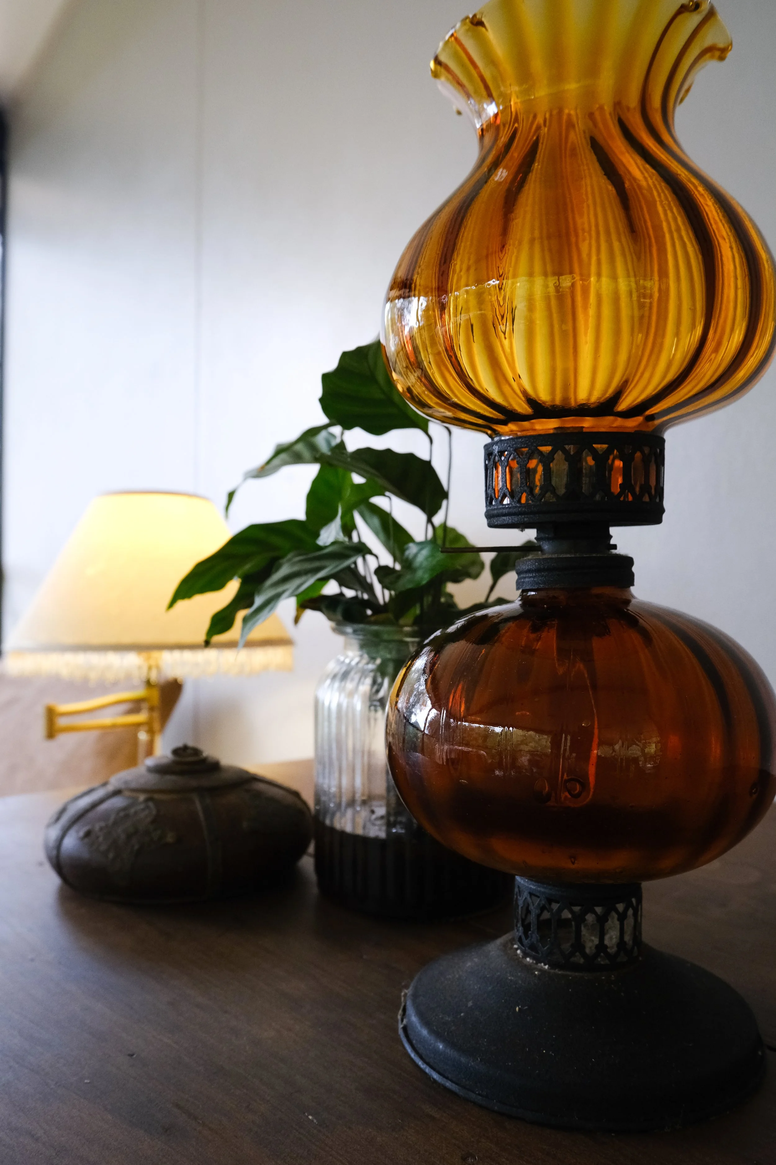Decorative amber-colored glass vases on a wooden surface with a plant and a table lamp in the background.