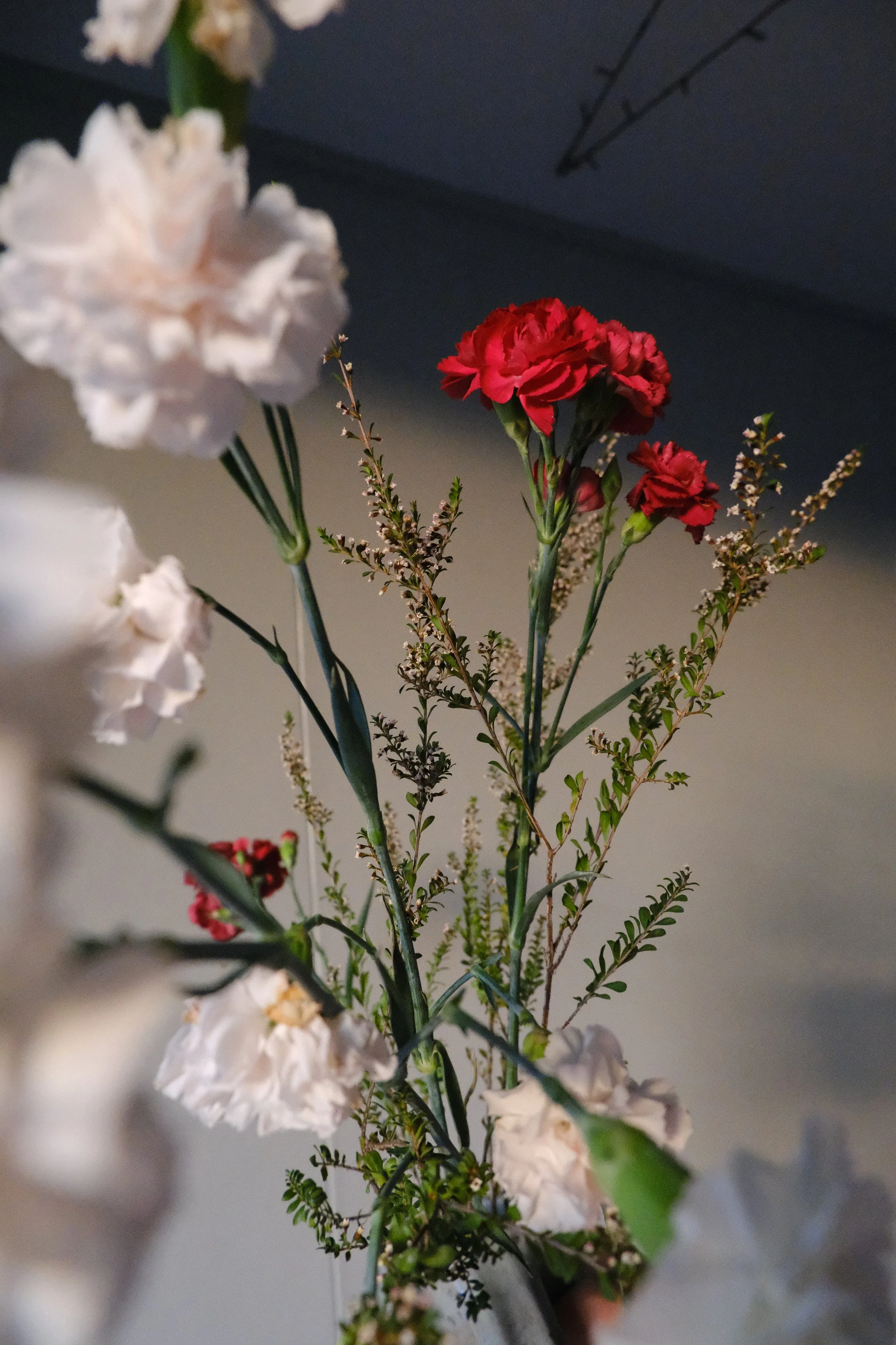 Close-up of a bouquet of mixed flowers including white, pink, and red blossoms with green foliage against a dark background.