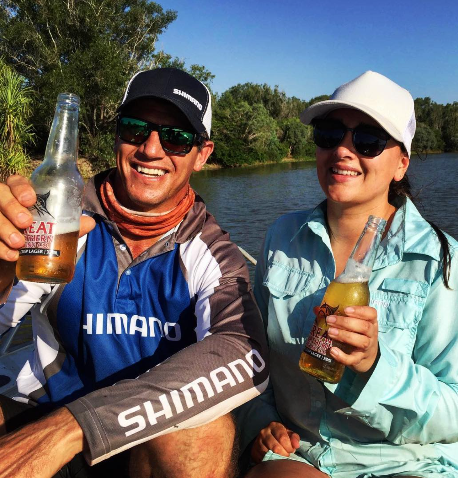 Two people aboard a boat during the Shimano x Million Dollar Fish campaign shoot, with a tropical riverbank behind them.