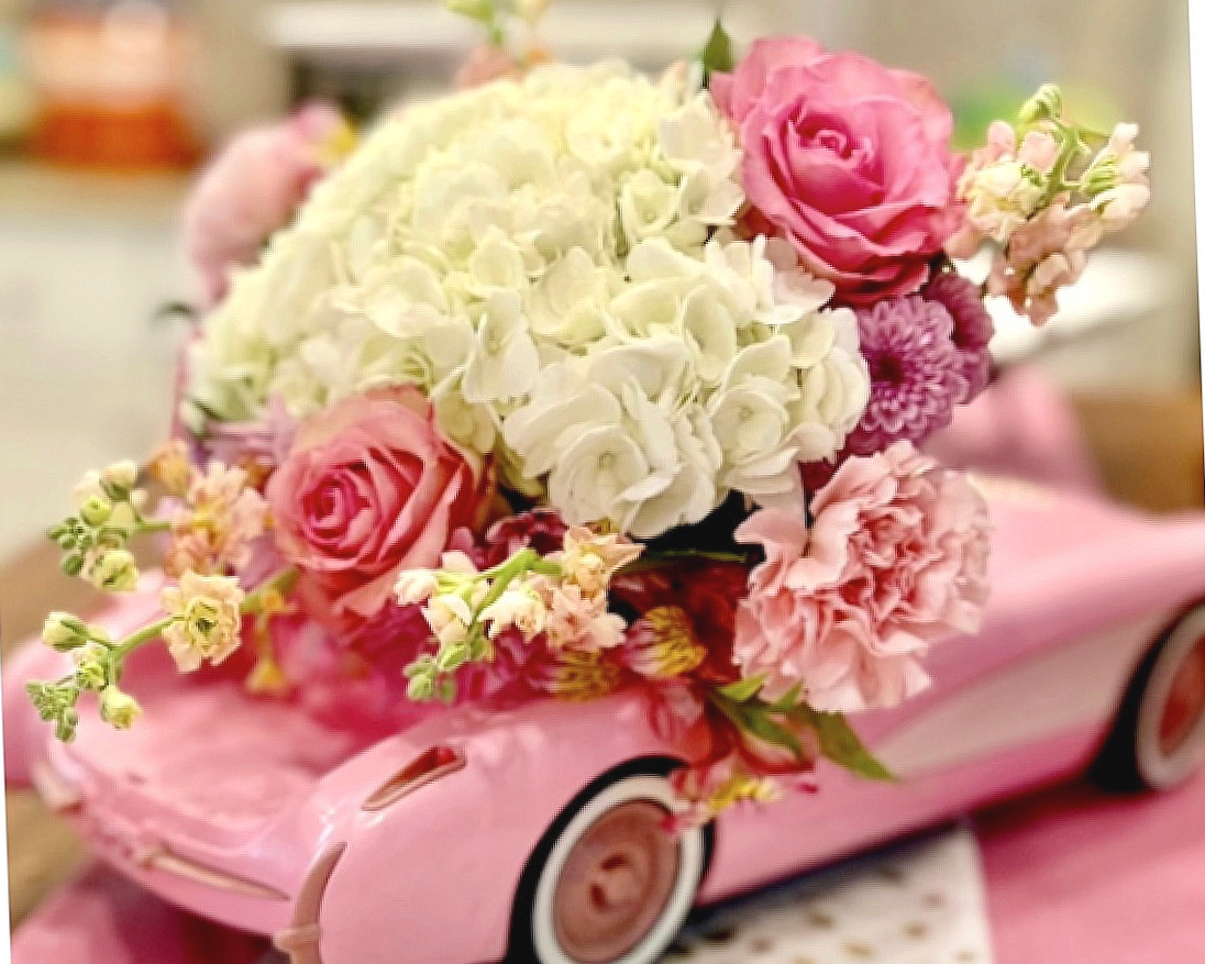 Pink toy car filled with a bouquet of pink, white, and purple flowers.