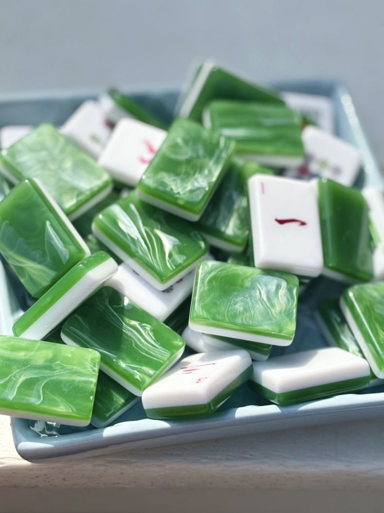 A white rectangular dish filled with green and white marble-patterned domino tiles, some with red pips, placed on a light-colored surface.