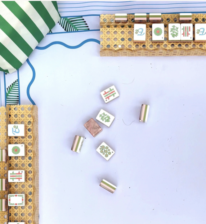 L-shaped board game with tiles featuring green, pink, and blue patterns, set on a white surface with striped and polka-dotted fabric in the background.