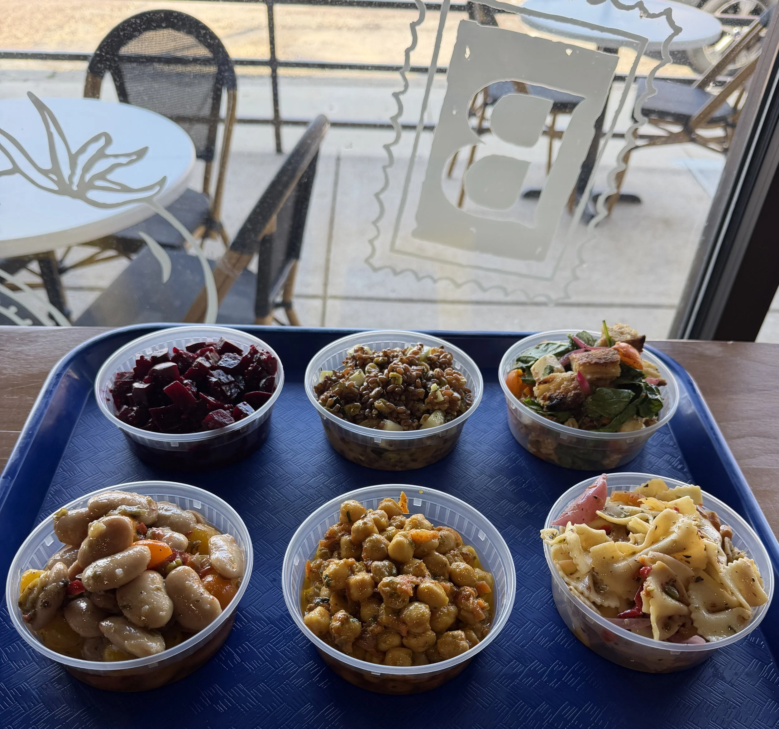 View of a tray with multiple bowls of various salads, seen through a window with decorative frosted glass designs.