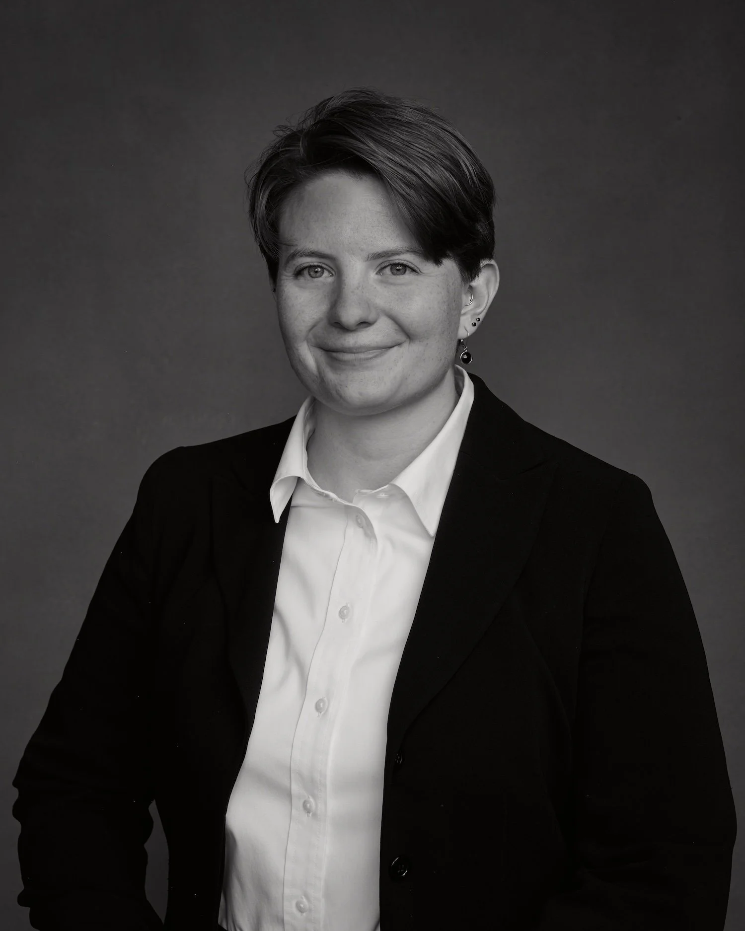 Black and white portrait of a woman with short hair, wearing a suit jacket and a white shirt, smiling slightly, against a plain dark background.