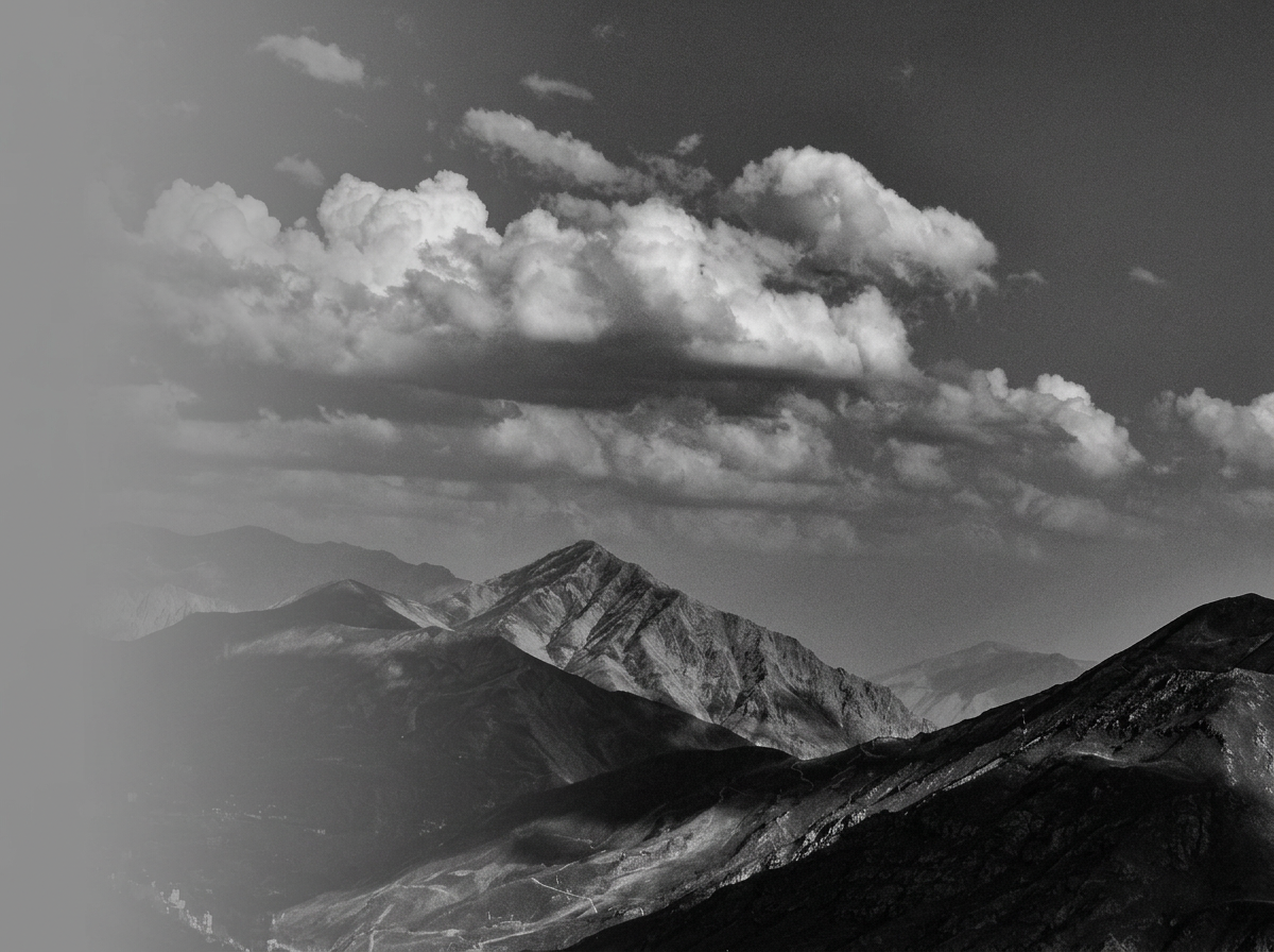 Black and white photograph of mountain peaks under a partly cloudy sky.