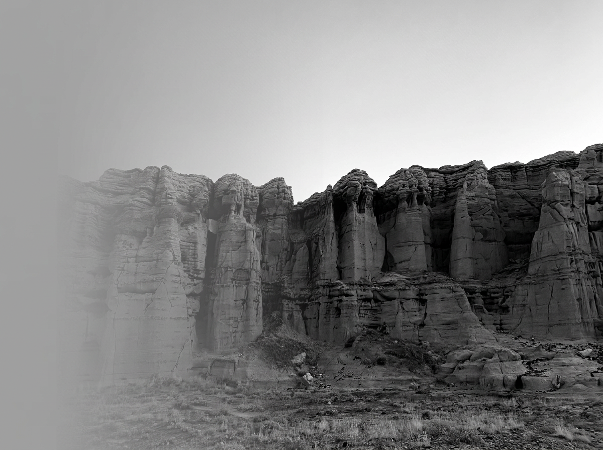 Black and white photo of a rocky cliff with layered formations and a clear sky.
