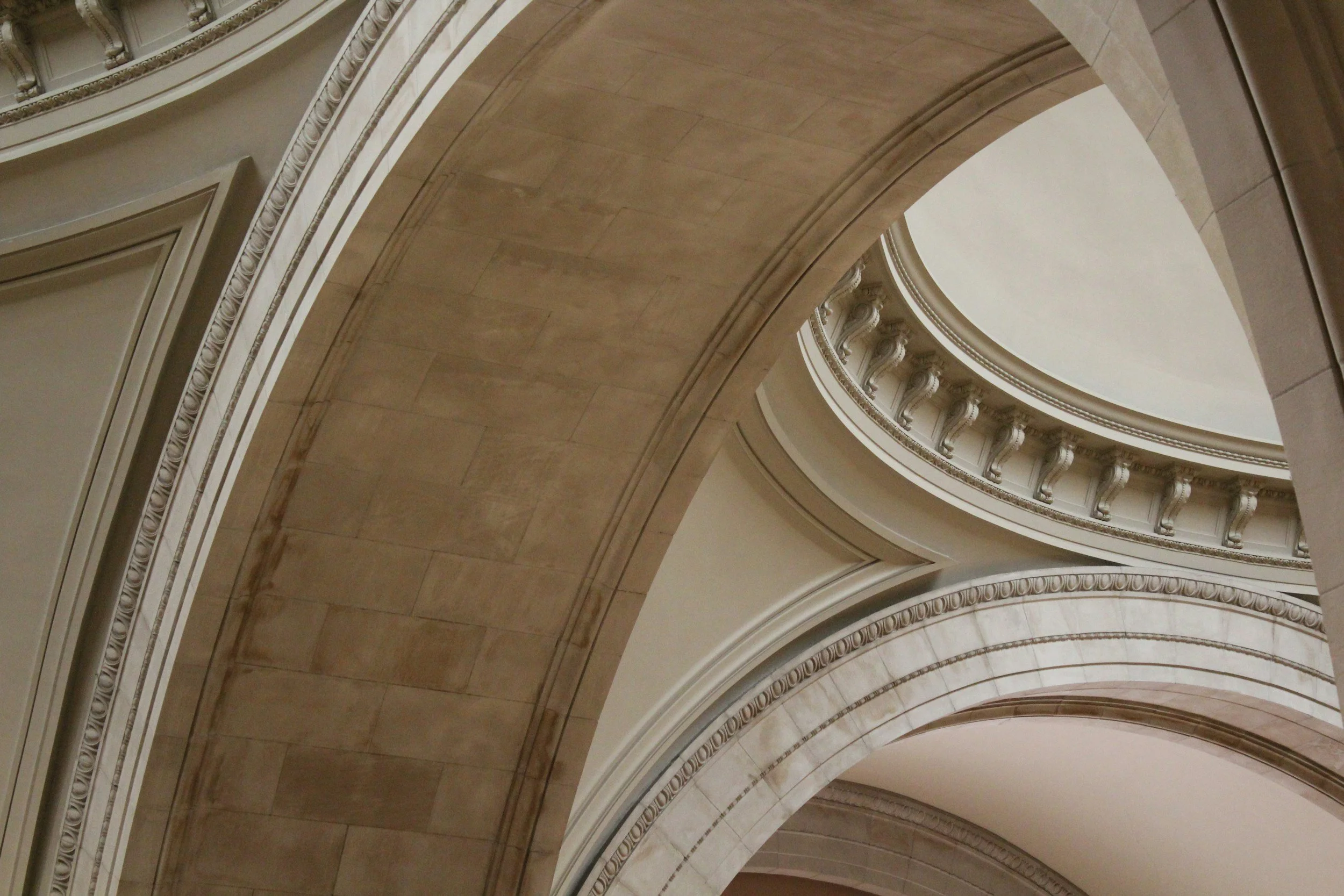 Interior view of a grand, ornate building with large, curved arches, decorative molding, and intricate architectural details.