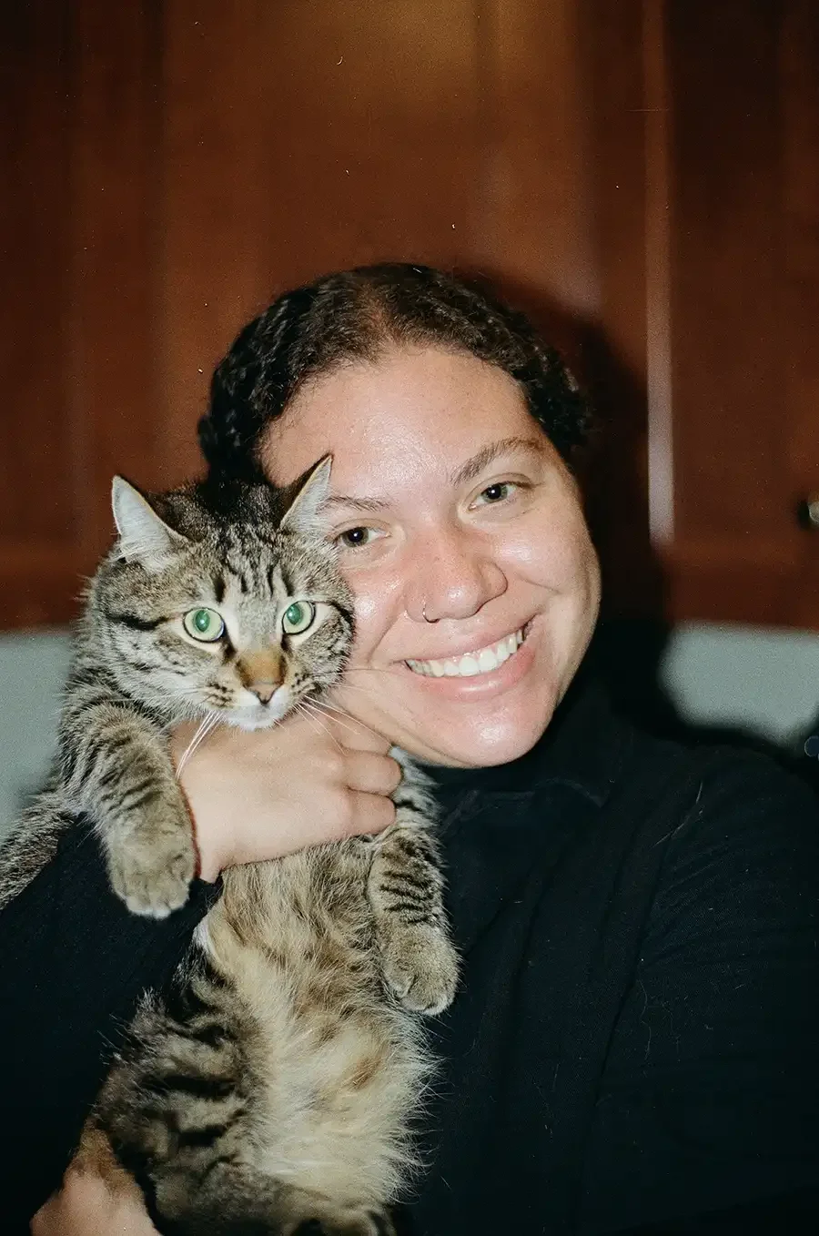 Photographer Zoe smiling while holding her tabby cat with green eyes close to her face.