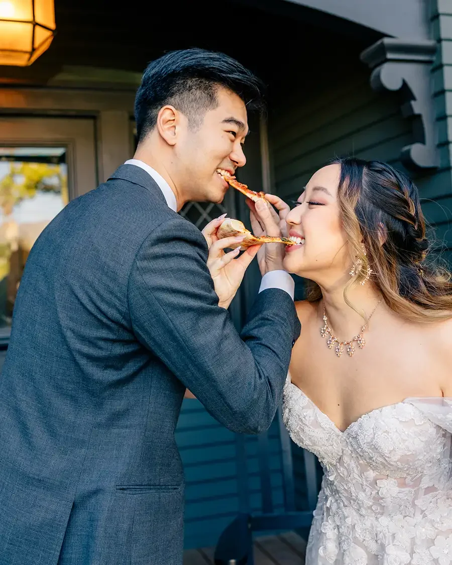 A wedding couple in formal attire sharing a slice of pizza together outside