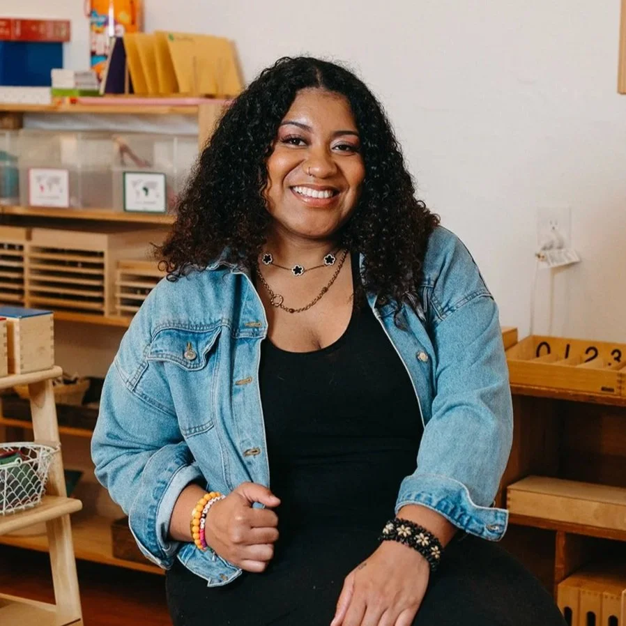Headshot of Little Eden Classroom Teacher, Téa, in the classroom sitting on a stool