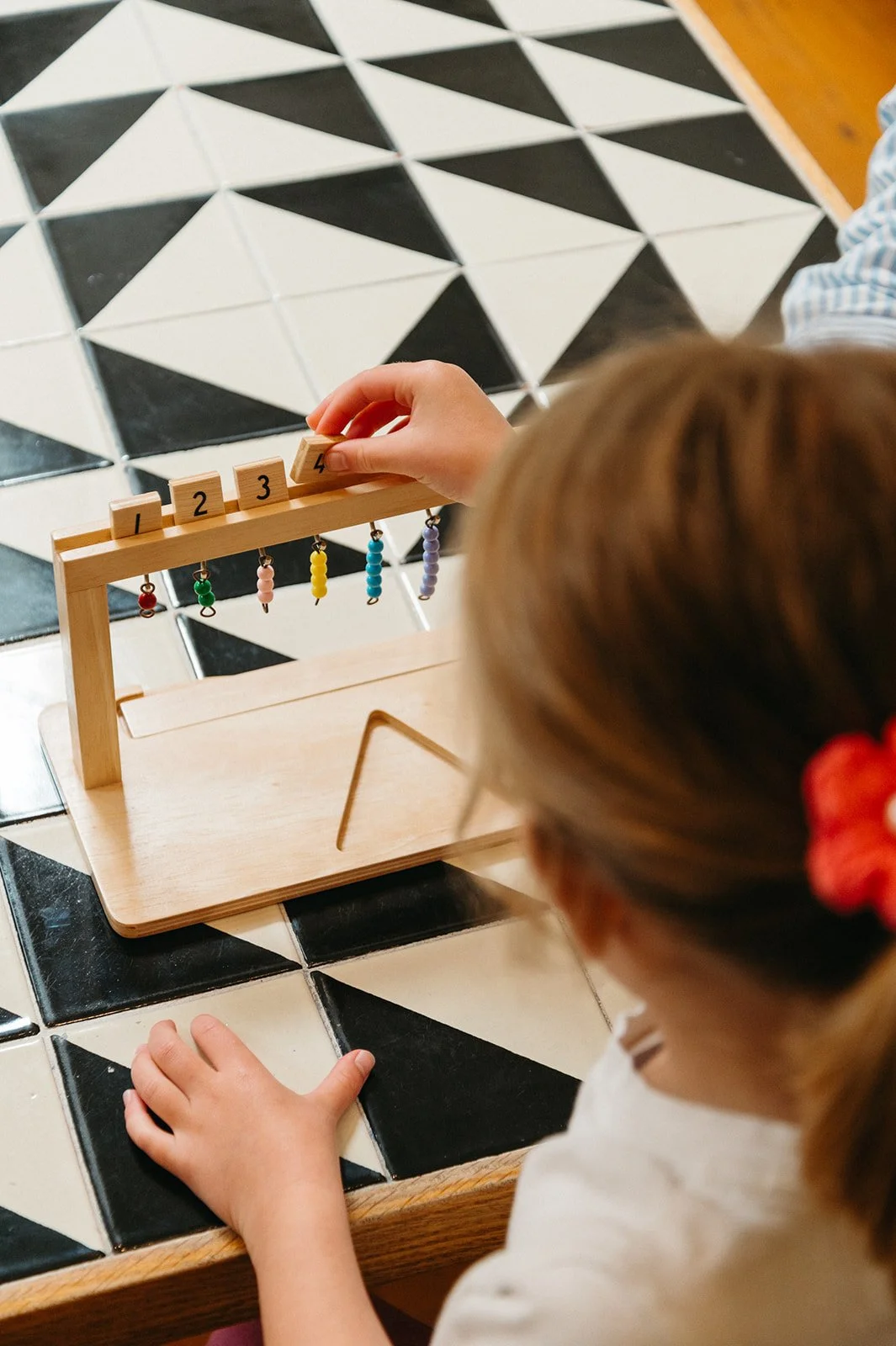 Preschooler placing wooden number tiles above matching bead bars on the Montessori bead stair, connecting numerals to quantities at Little Eden Montessori preschool in San Francisco