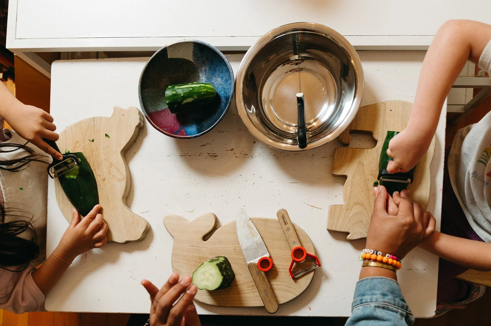 Overhead view of children slicing cucumber on wooden cutting boards, a Montessori practical life activity