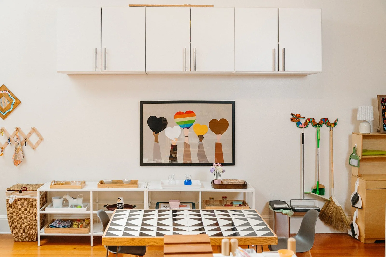 Little Eden Montessori preschool in San Francisco, with low shelves of hands-on Montessori materials, a framed print of raised hands holding colorful hearts, and a tiled work table