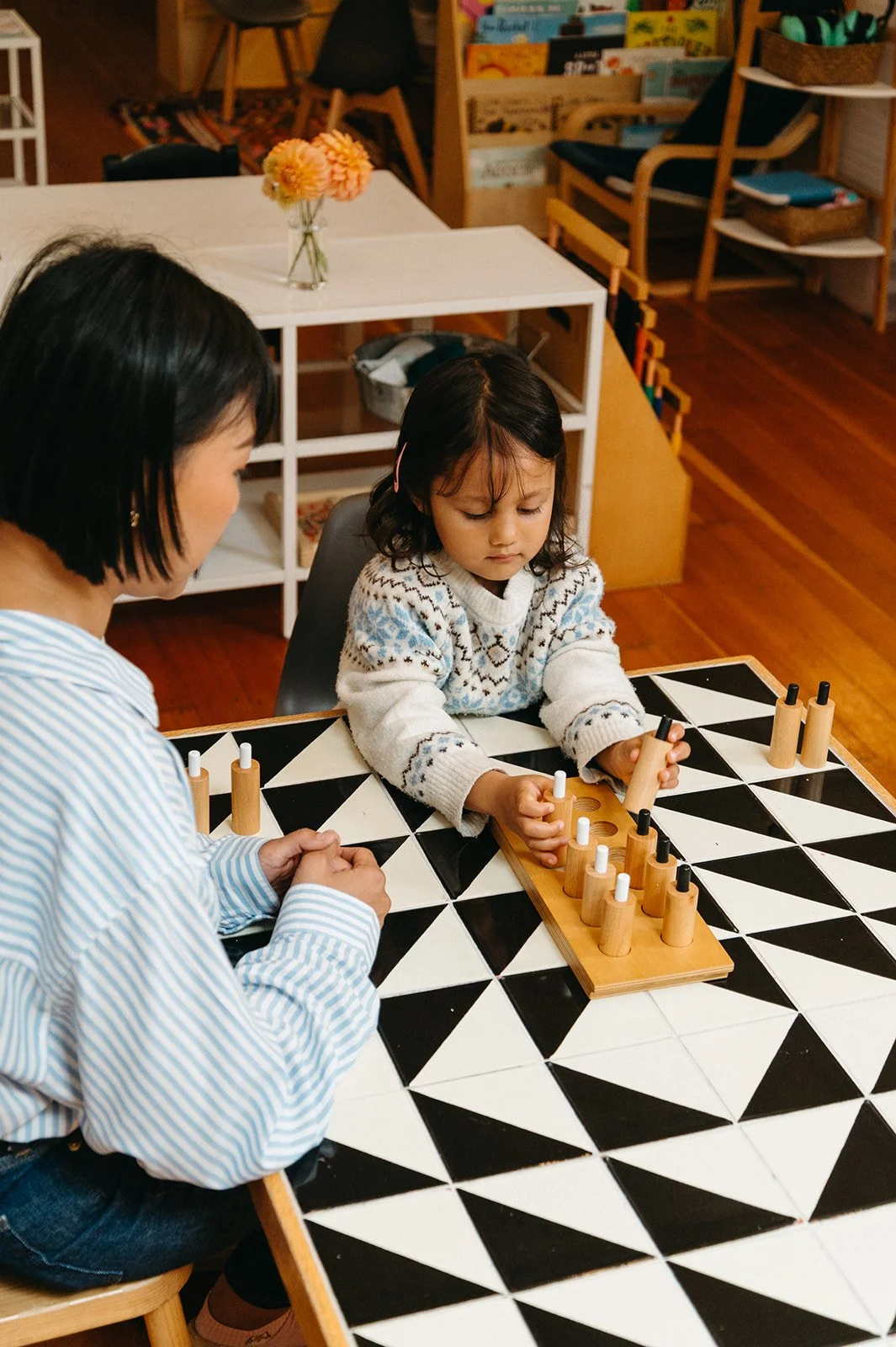Montessori teacher watching as a preschooler fits wooden knobbed cylinders into a block, a sensorial material that builds concentration and fine motor skills at Little Eden Montessori preschool in San Francisco