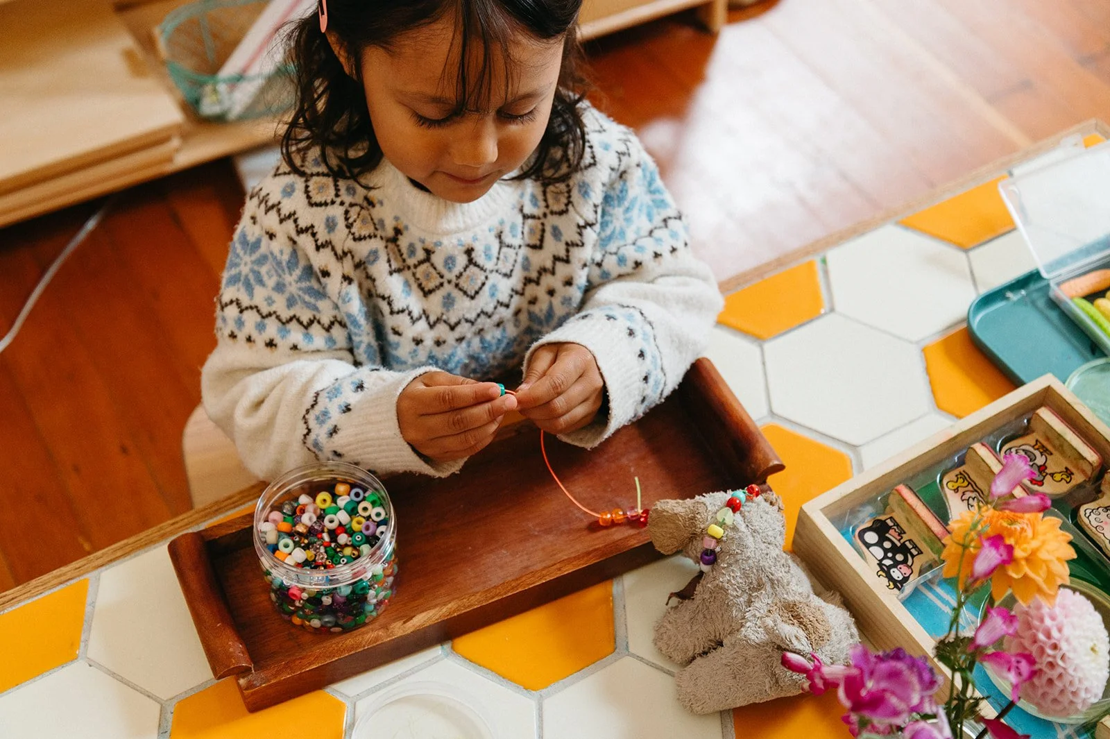 Preschooler threading colorful beads from a wooden tray, building fine motor skills and concentration