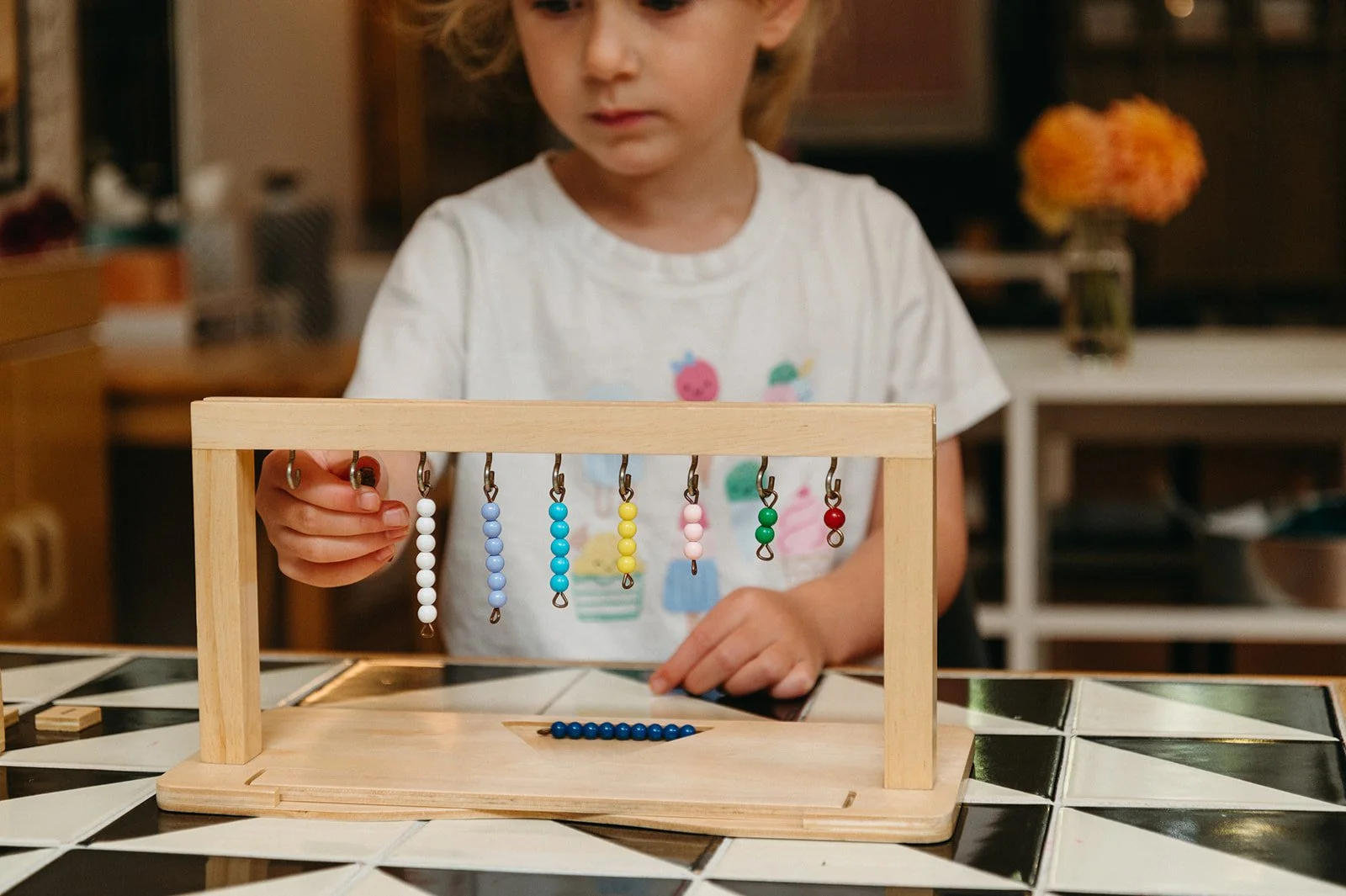 Preschooler hanging colorful bead bars on a wooden stand while using the Montessori bead stair, a hands-on math materia