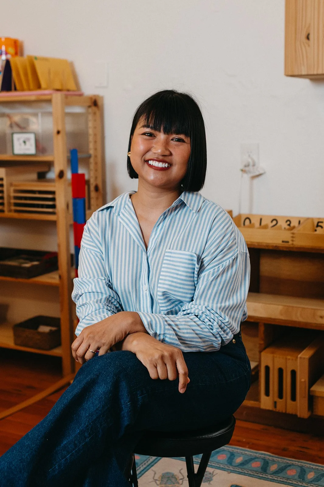 Headshot of Little Eden Montessori teacher, Natty, in the classroom sitting on a stool