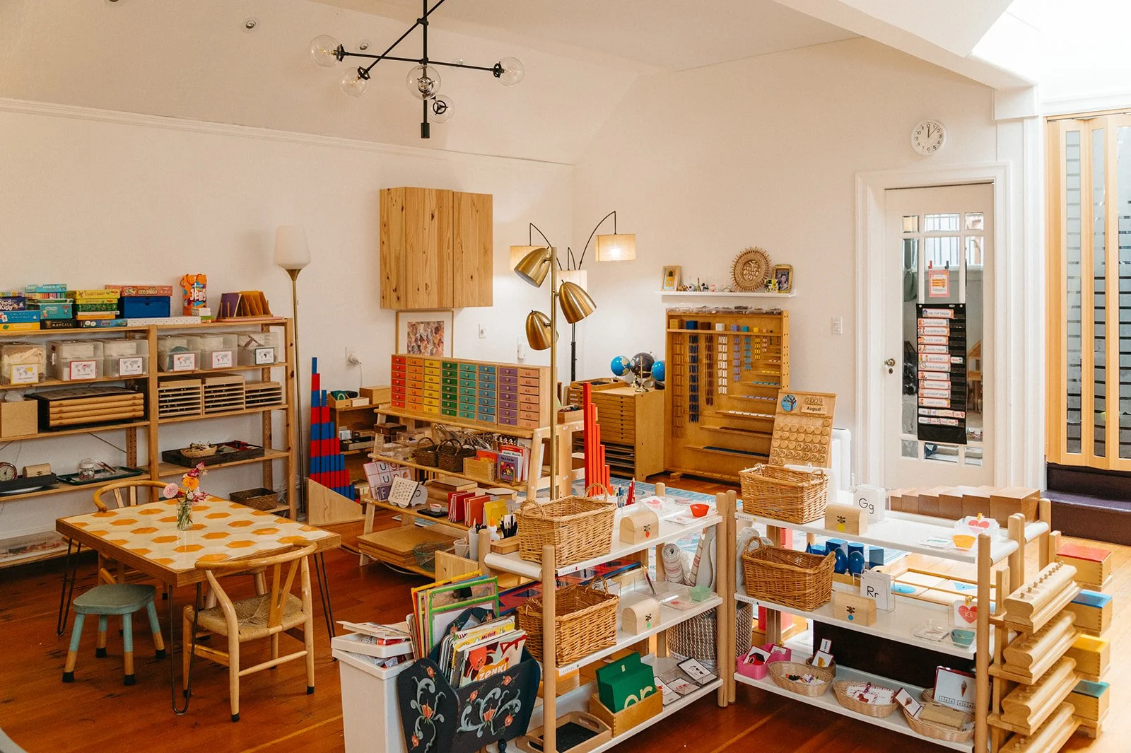 Bright Montessori classroom at Little Eden in San Francisco, with wooden shelves of hands-on materials, woven baskets, and child-sized tables