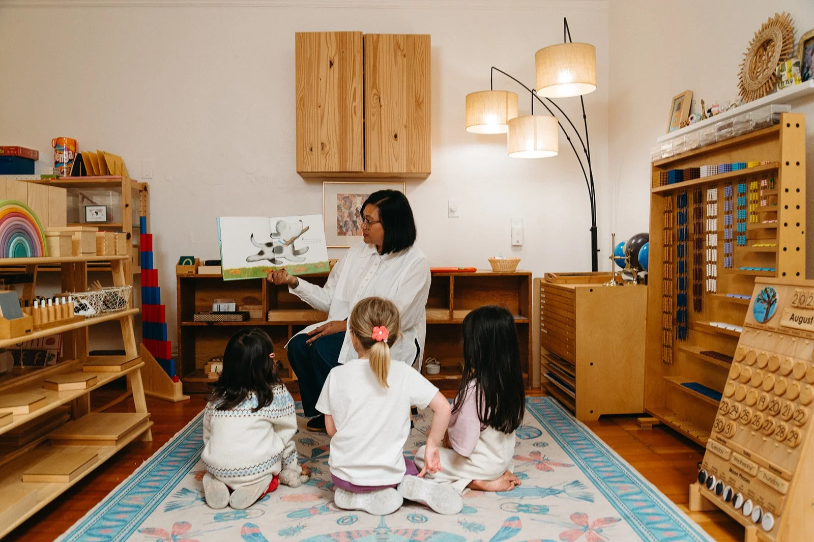Teacher leading a small group lesson as three children sit together on a rug in the Montessori classroom