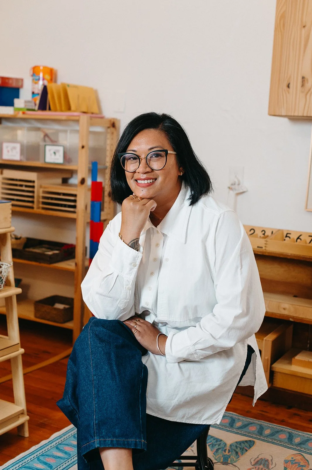 Headshot of Little Eden Preschool Director, Michelle San Agustin, in the classroom sitting on a stool