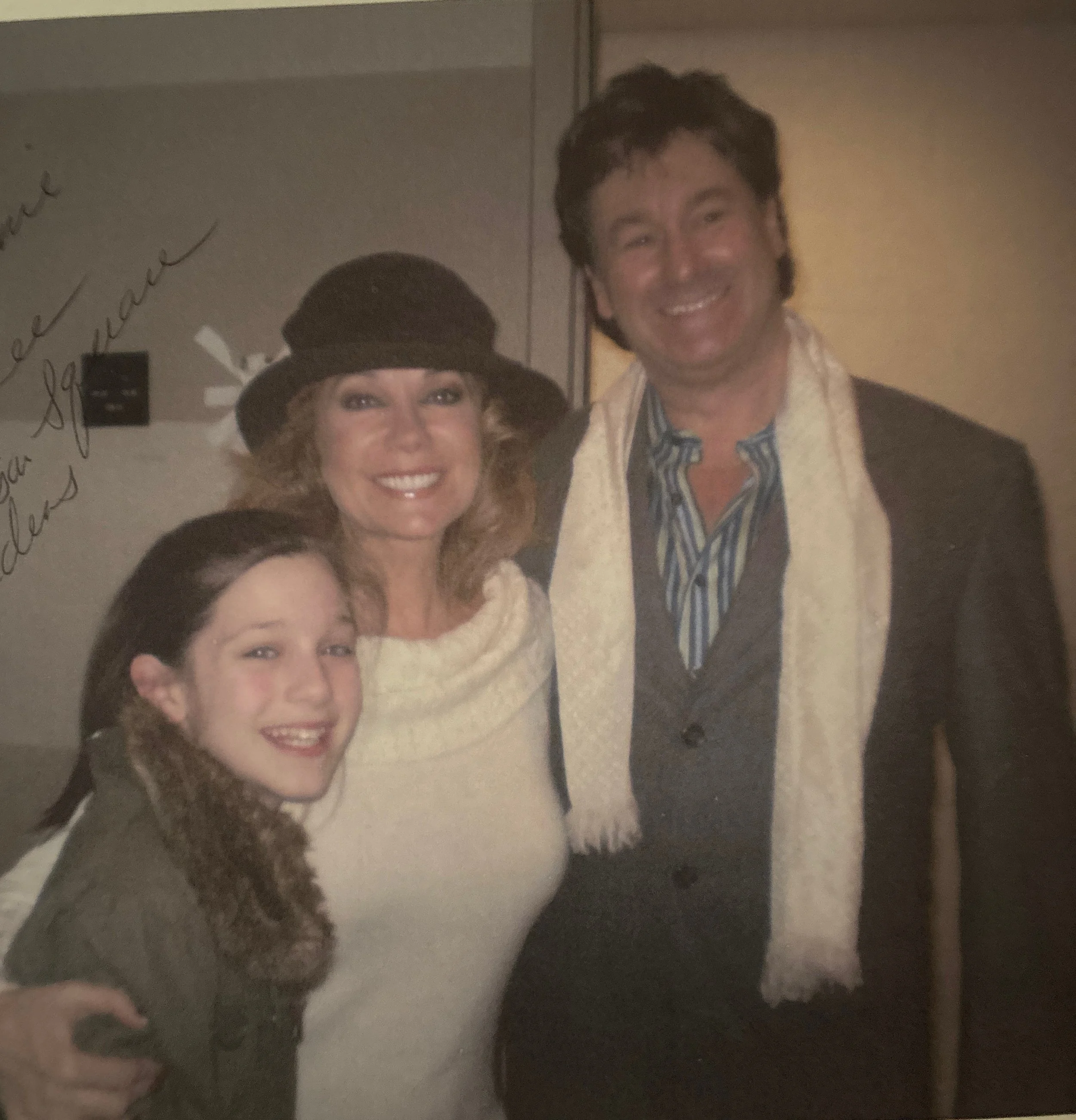 A woman and a man smiling for a photo, with the woman wearing a large hat and the man wearing a jacket and striped shirt.