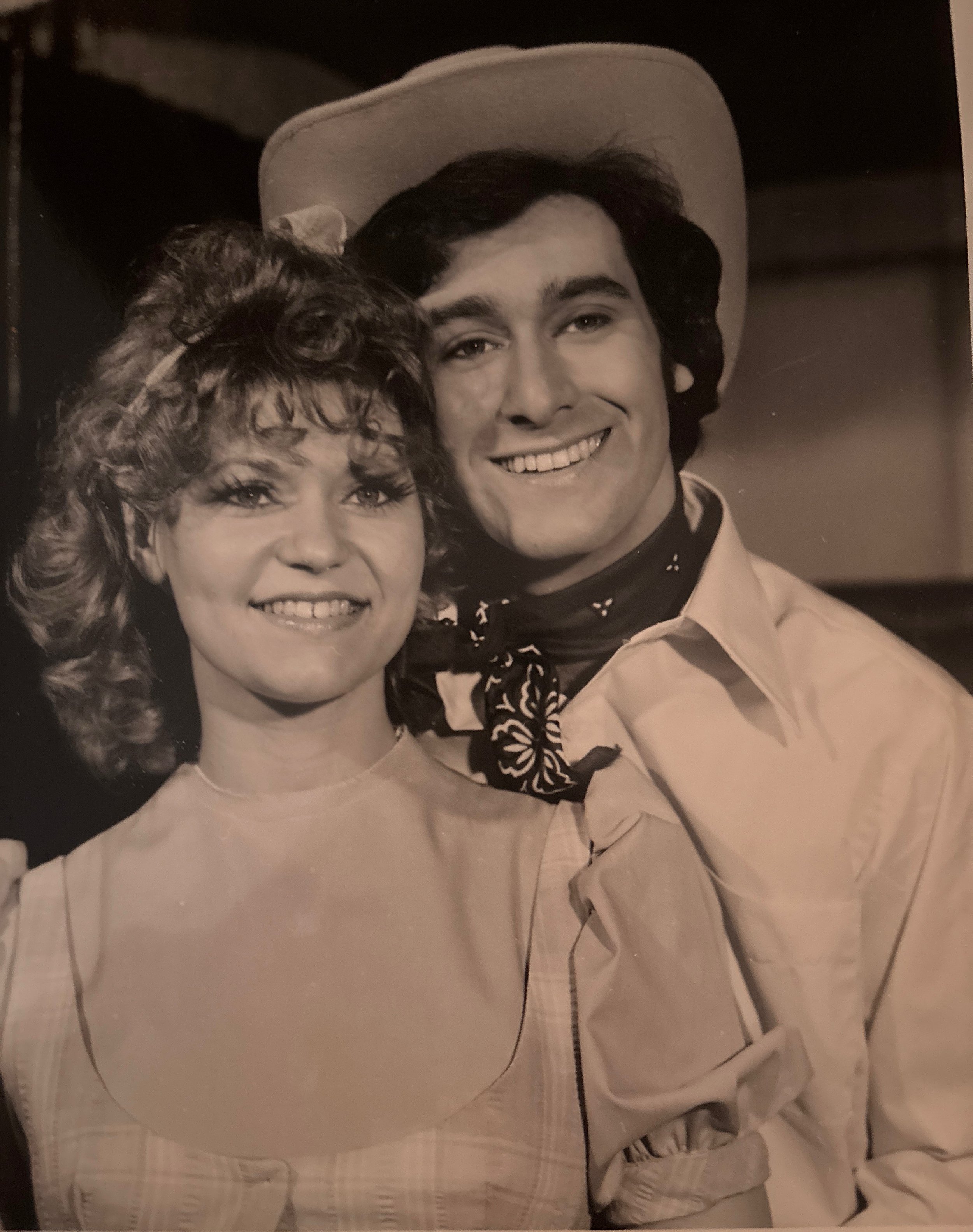 Black and white photo of a man and a woman smiling and close together, wearing Western-style hats and cowboy shirts.
