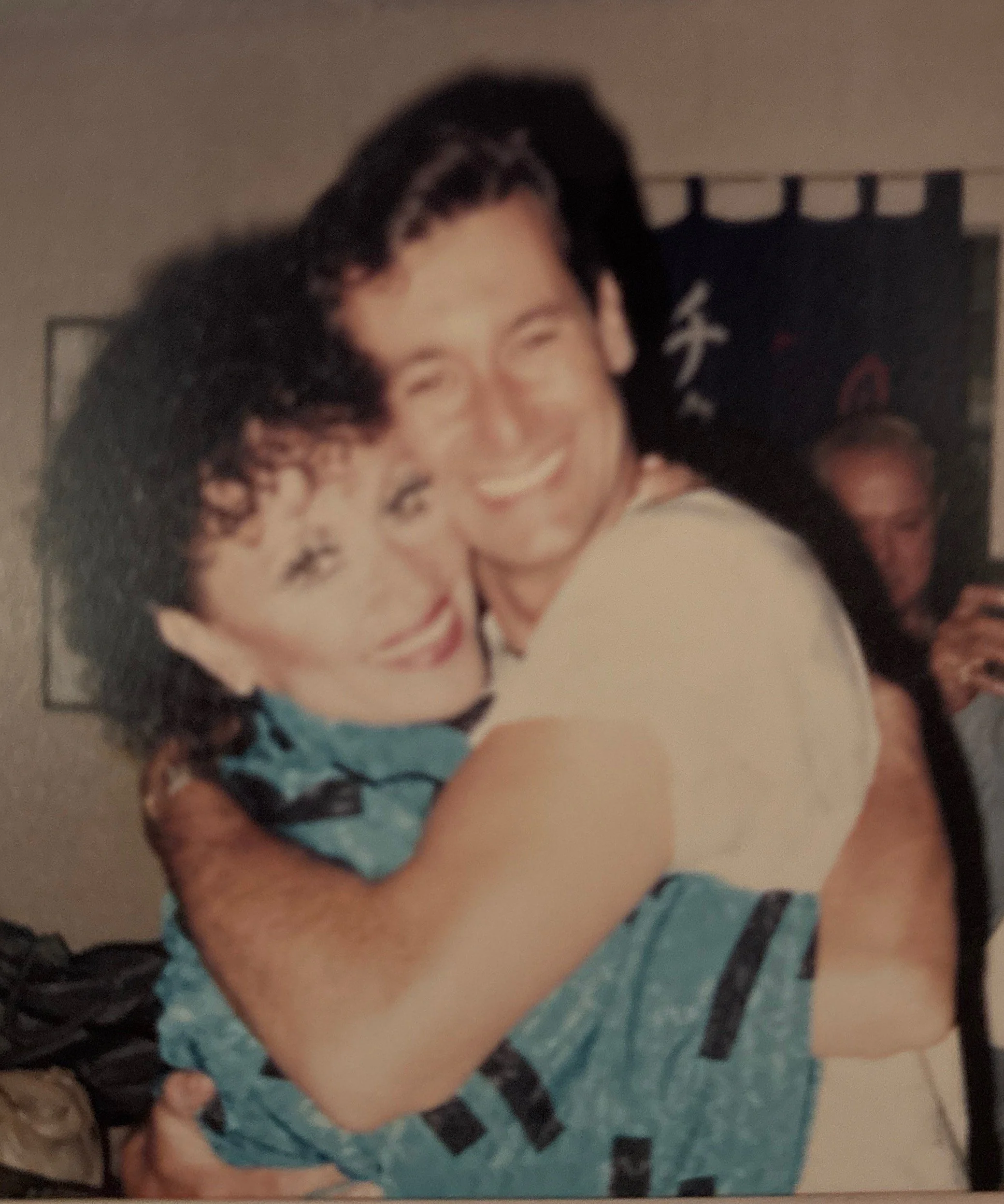 A smiling woman hugging a child with curly hair, wearing a blue and black striped shirt.