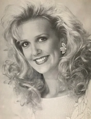 Black and white photo of a woman with voluminous curly hair, wearing large flower-shaped earrings and a sparkling top.