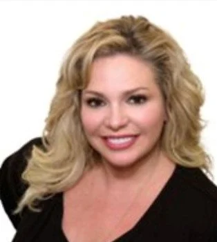 A woman with blonde, curly hair smiling, wearing a black top against a white background.