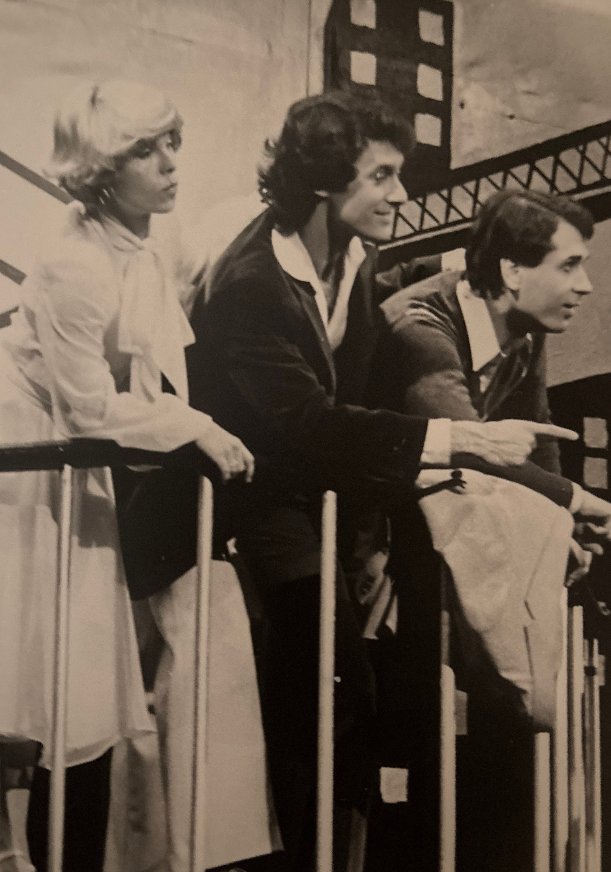 Three people sitting on a bench, looking in the same direction, with part of a railing visible in the foreground and a wall behind them.