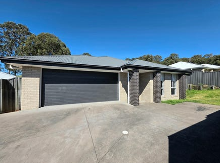 A single-story house with a gray garage door, brick exterior, and a concrete driveway, under a clear blue sky.