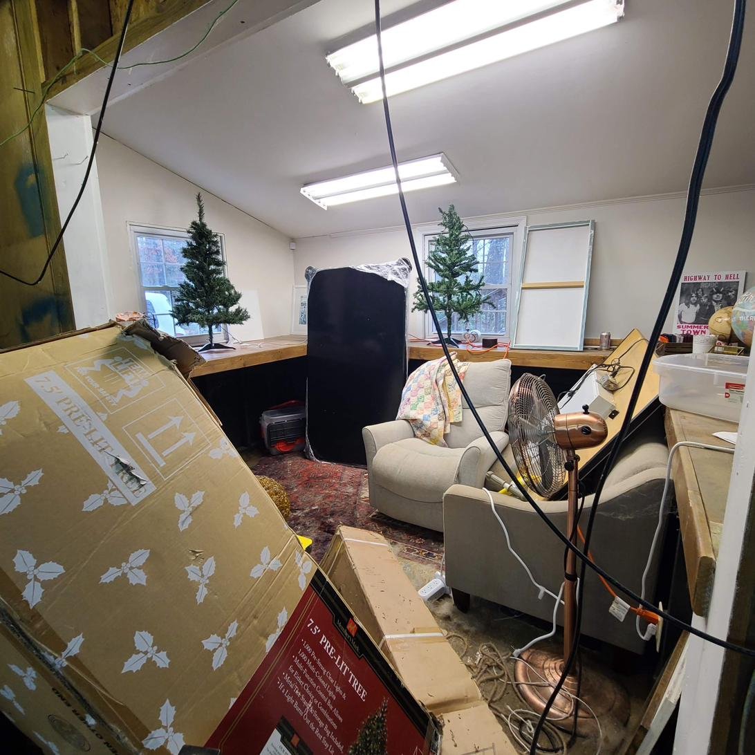 Cluttered room mid-holiday cleanout in Memphis, TN, with two small Christmas trees, a covered armchair, and boxes ready for junk removal.