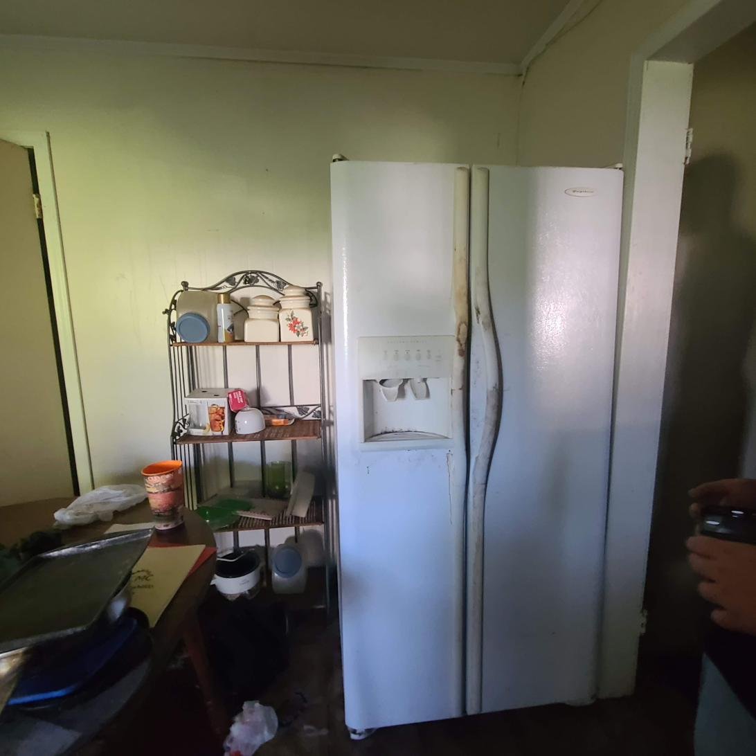Rusted side-by-side refrigerator in a cluttered kitchen before an appliance removal service in Memphis, TN.