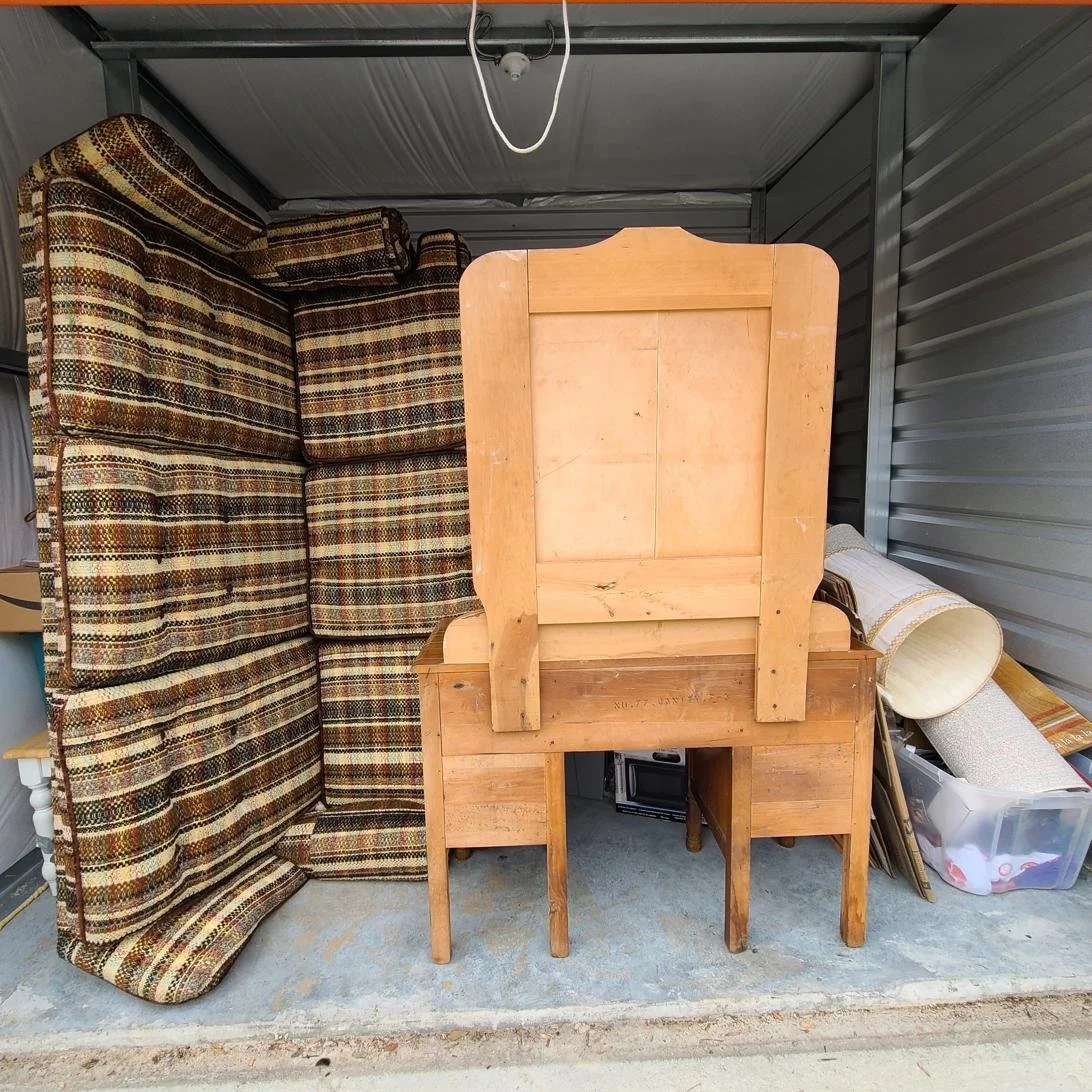 Disorganized storage unit with furniture and rolled carpet before a full cleanout service in Memphis, TN.