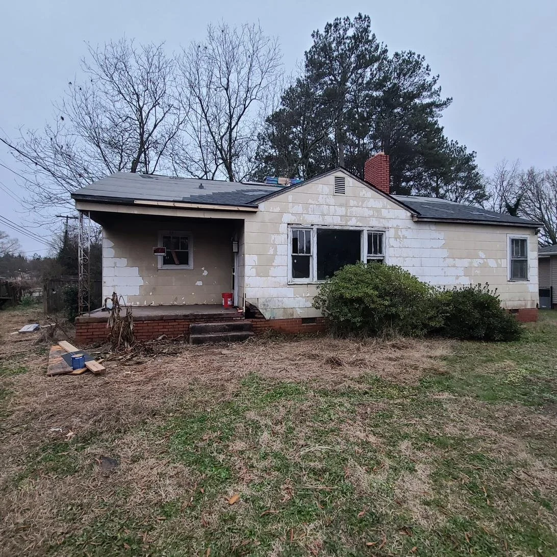 Before junk removal in Memphis, TN — an older home with peeling paint, a damaged brick porch, broken windows, and an overgrown yard in need of a full property cleanout.