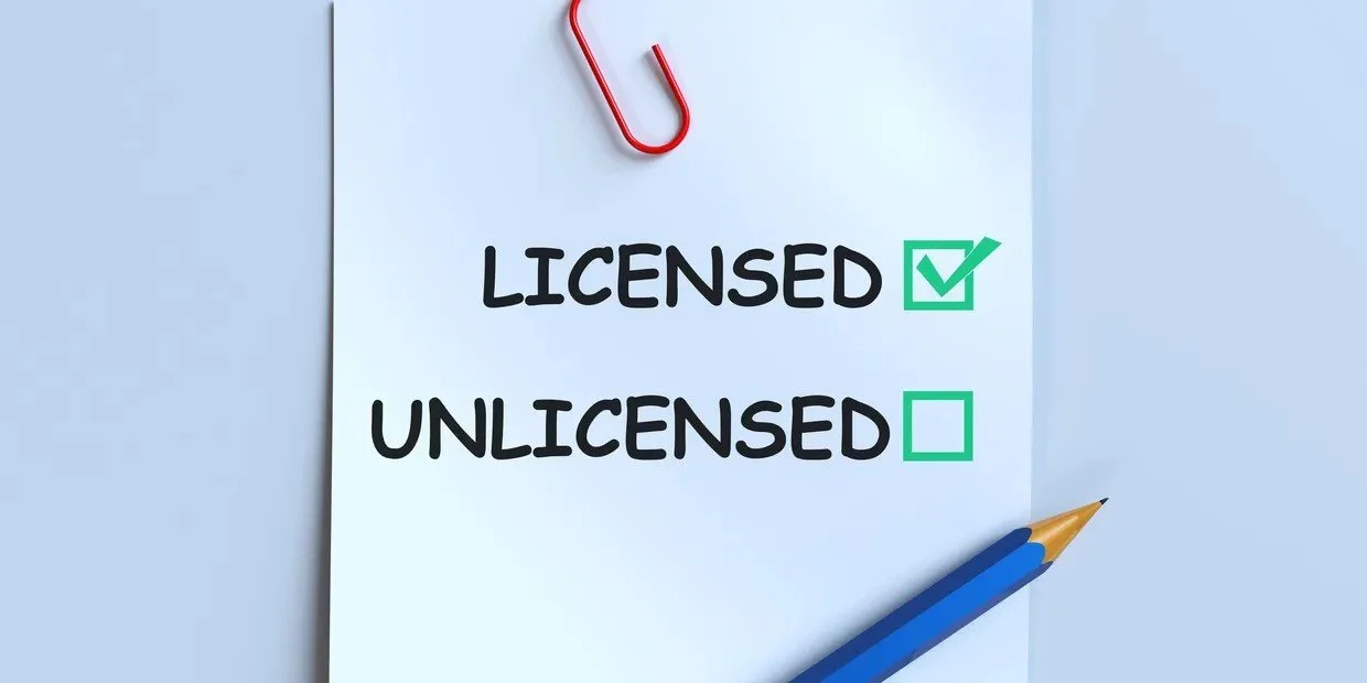 A white sheet of paper with the words 'LICENSED' and 'UNLICENSED', with a green check mark next to 'LICENSED' and a green empty box next to 'UNLICENSED'. A red paperclip is attached to the top of the paper and a blue pen is resting at the bottom right corner.