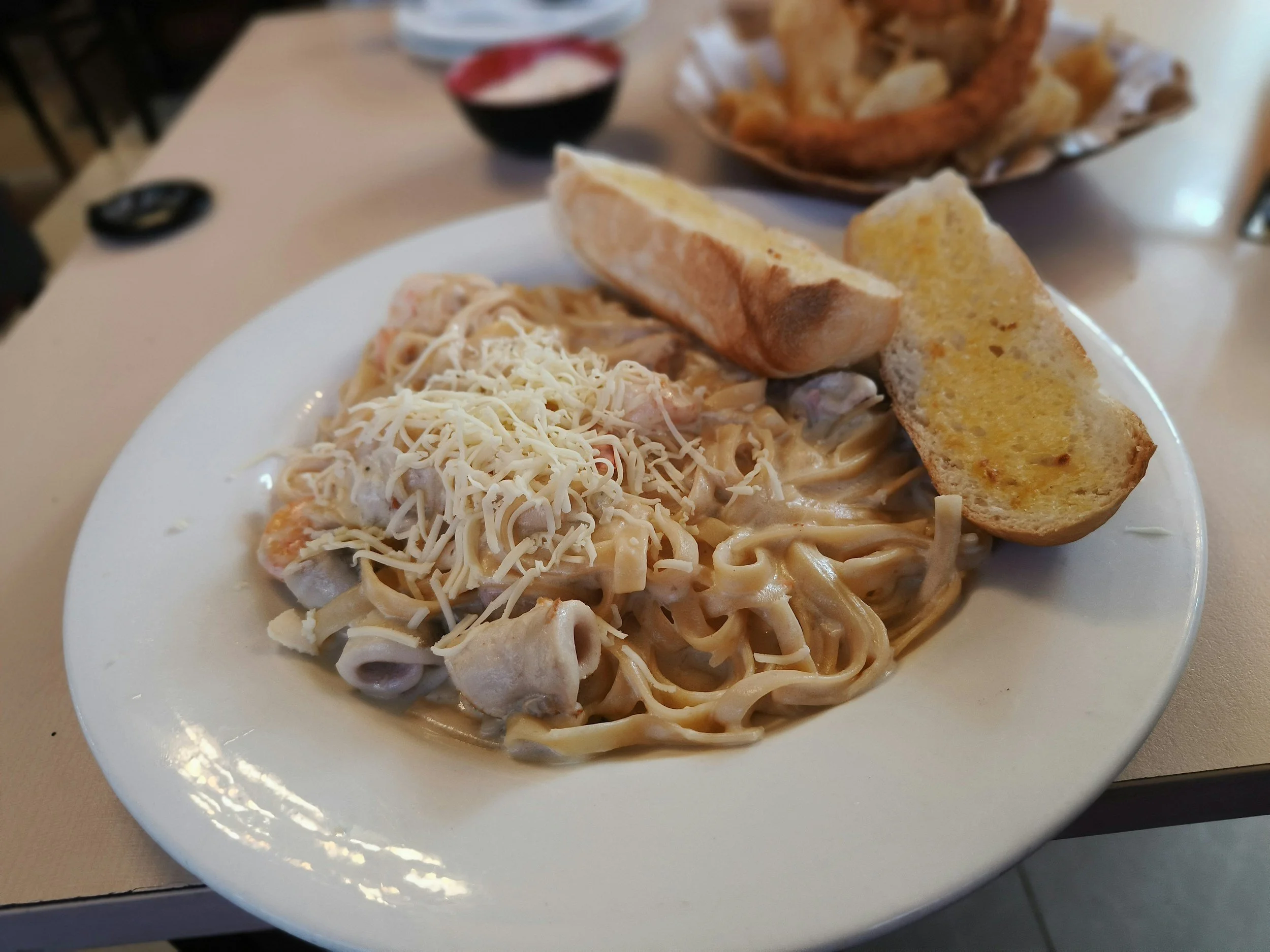 A plate of fettuccine pasta with creamy sauce, topped with grated cheese, served with slices of garlic bread.