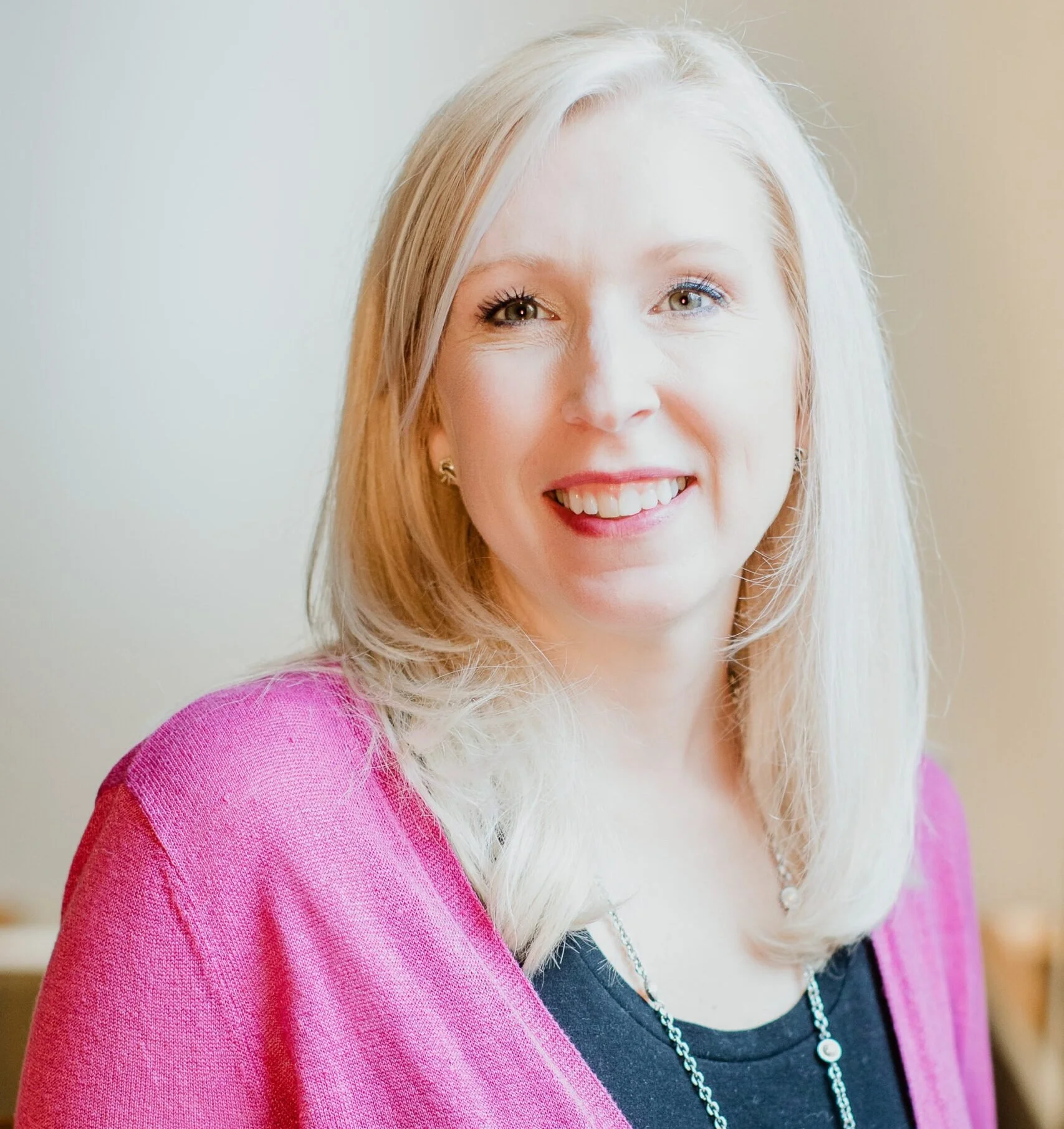 A woman with blonde hair wearing a pink sweater and smiling.