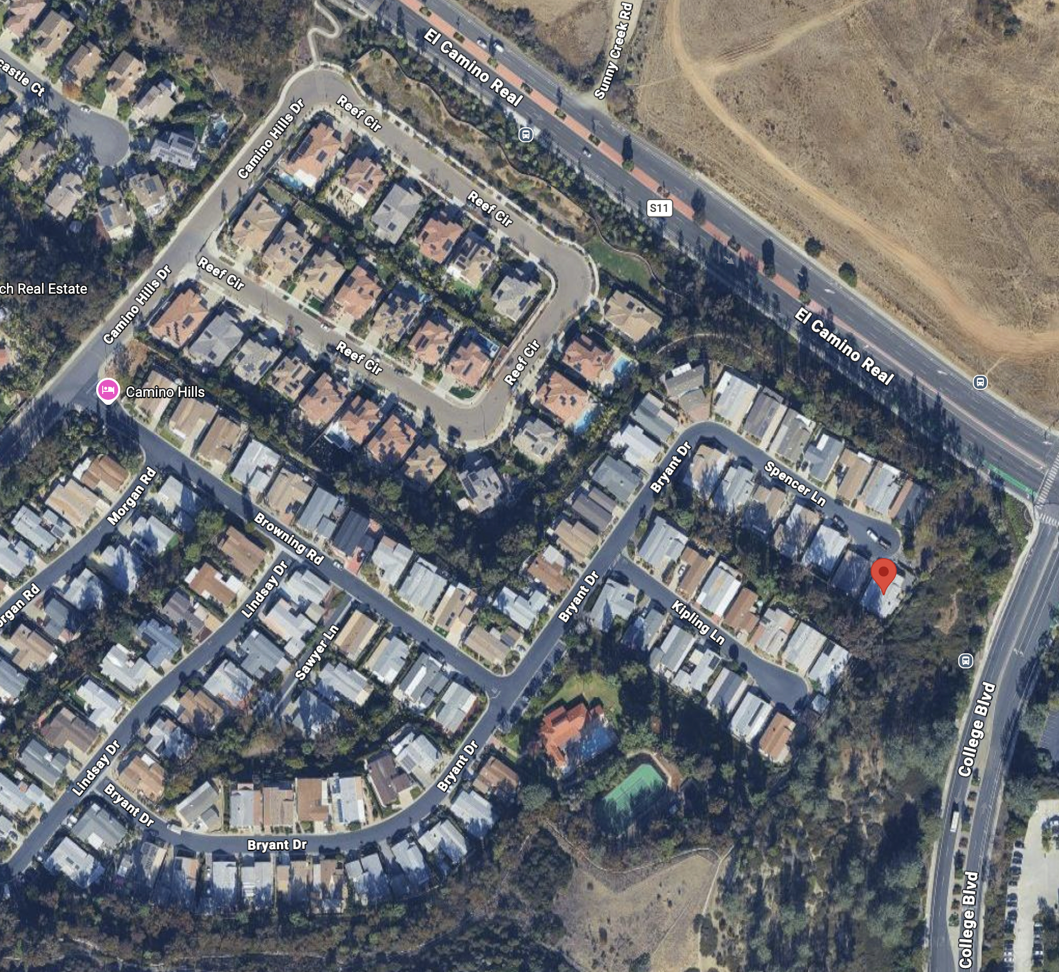 Aerial view of a neighborhood with houses, streets, and a nearby highway with vehicles. The streets are named Camino Hills Dr, Reef Cir, Bryan Dr, Lindsay Dr, and college Blvd.